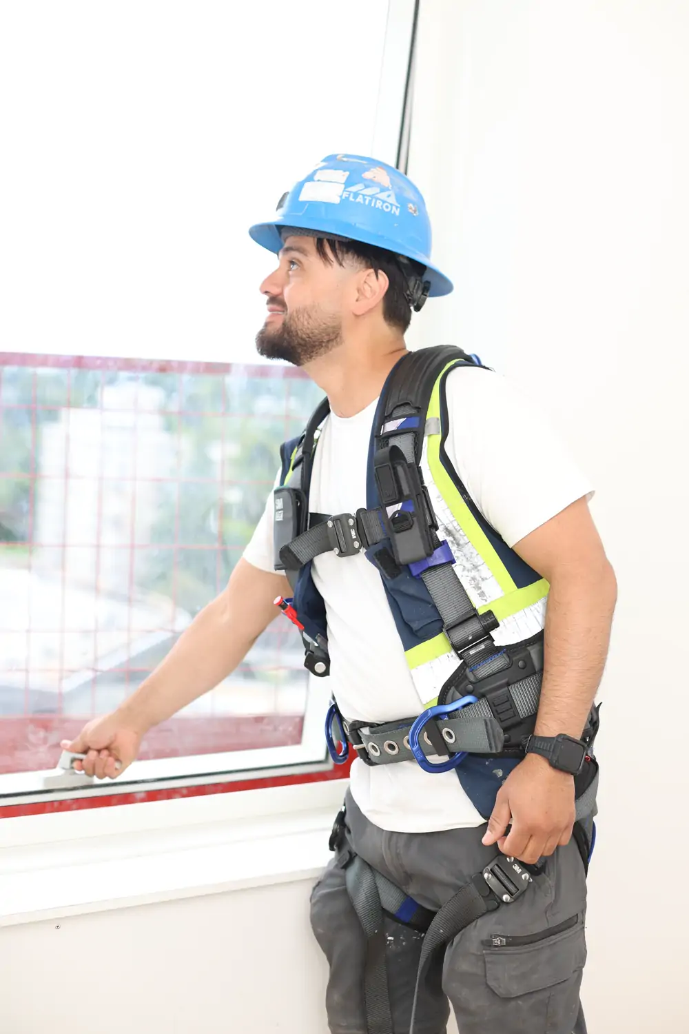 Worker in a fall-arrest harness checking a window opening on an upper floor